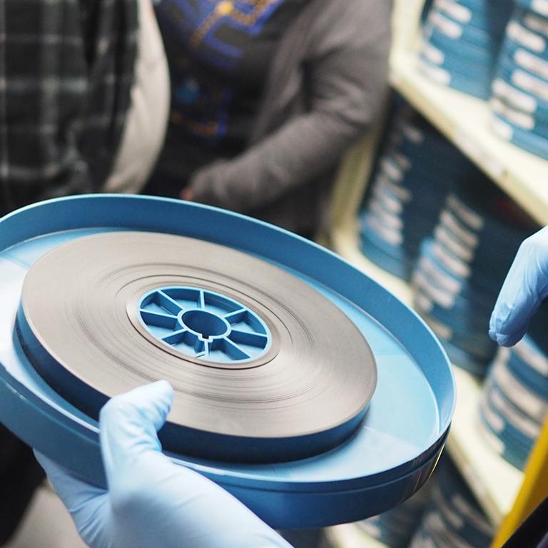 Close up of a person's gloved hands holding a canister with a reel of film in it.